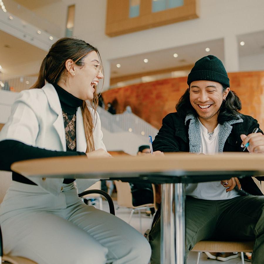 Two students talk at table in Uhall.